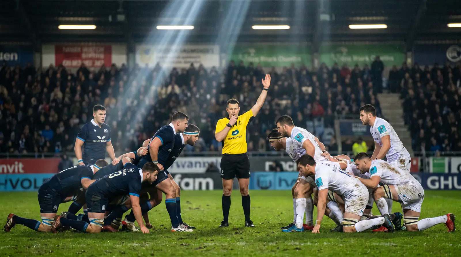 Rugby referee signalling during a professional match under floodlights